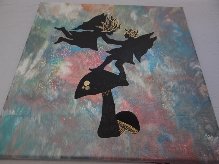 Angled shot of a 12"x12" acrylic pour painting featuring black silhouetted fairies with gold embellishments dancing on a mushroom, set against a swirling, ethereal background.
