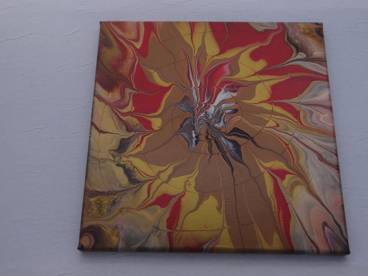 A 12"x12" acrylic pour painting featuring a radiant burst of gold, bronze, and red with black and white details by Blue St Designs.