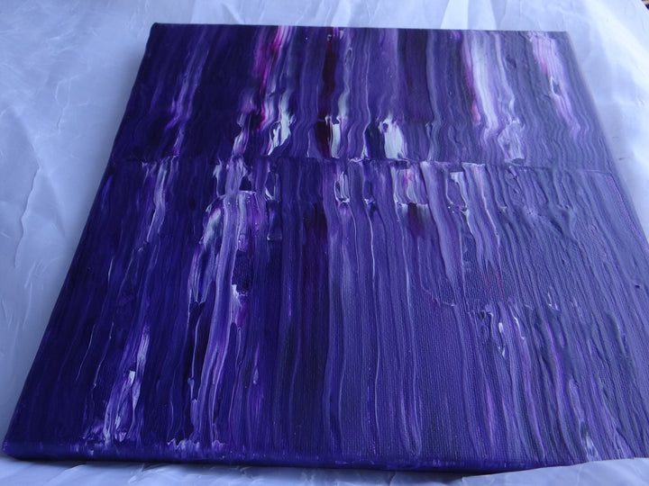 Close-up angled view of Purple Stripe, a 10"x10" acrylic pour painting with deep violet hues, black accents, and streaks of white. The swipe technique creates a fluid, textured effect, highlighting the rich layering of colors.