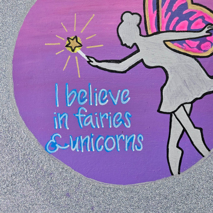 Detail of the phrase 'I believe in fairies & unicorns' in bright blue lettering on the Fairies & Unicorns acrylic painting.